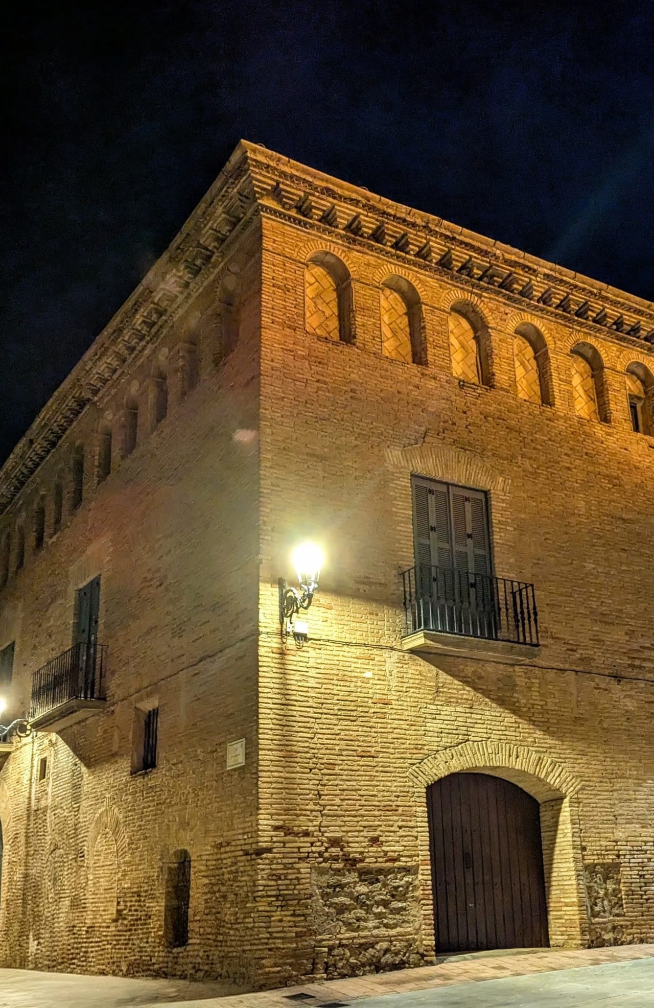 Un edificio antiguo iluminado de ladrillo con balcones y una puerta de madera en una calle oscura.