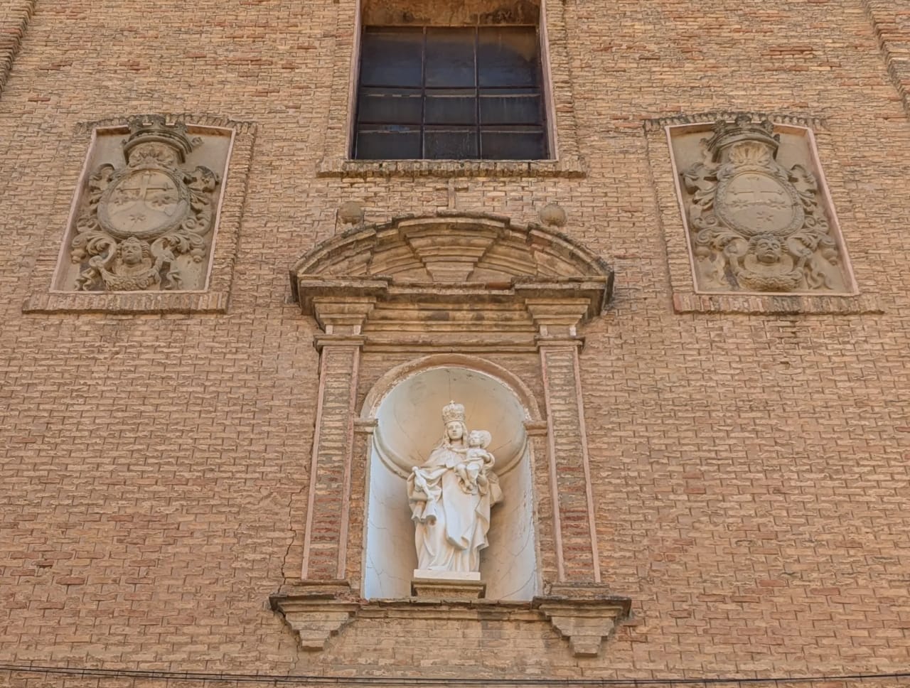 Escultura de la Virgen María con el niño Jesús en hornacina de arco, en fachada de ladrillo.