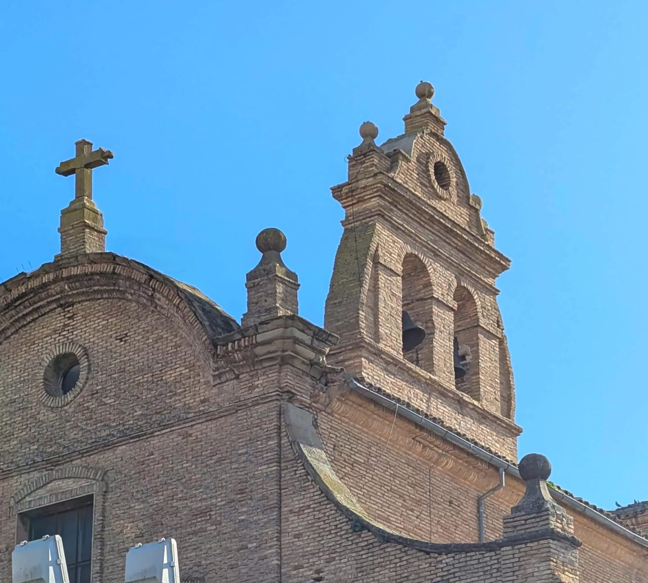 Torre de iglesia de ladrillos con cruz y campanario bajo cielo azul.