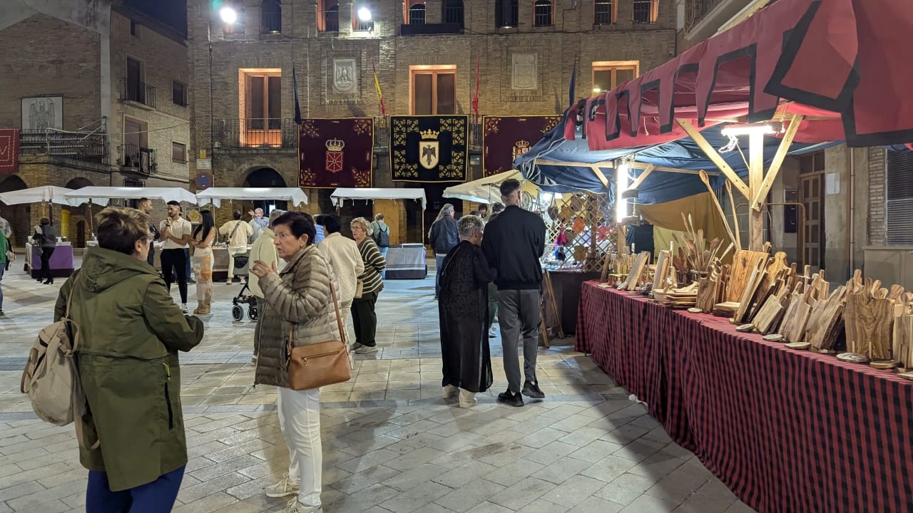 Mercado nocturno en una plaza histórica con gente paseando y productos de madera.