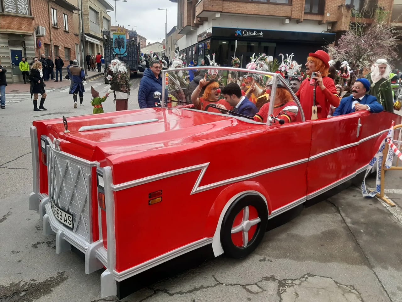 Un auto rojo con personas disfrazadas en un desfile por la calle.
