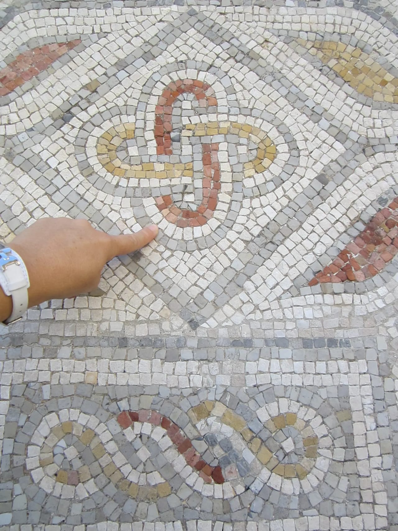 Mosaico de piedra con diseño geométrico y mano apuntando.