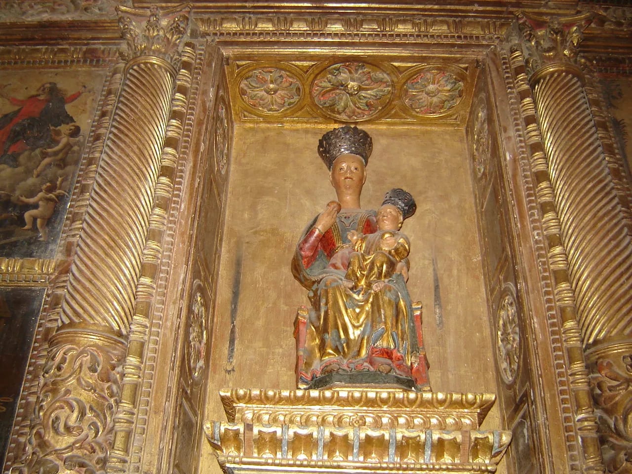 Estatua de la Virgen María con el niño Jesús en un retablo dorado.