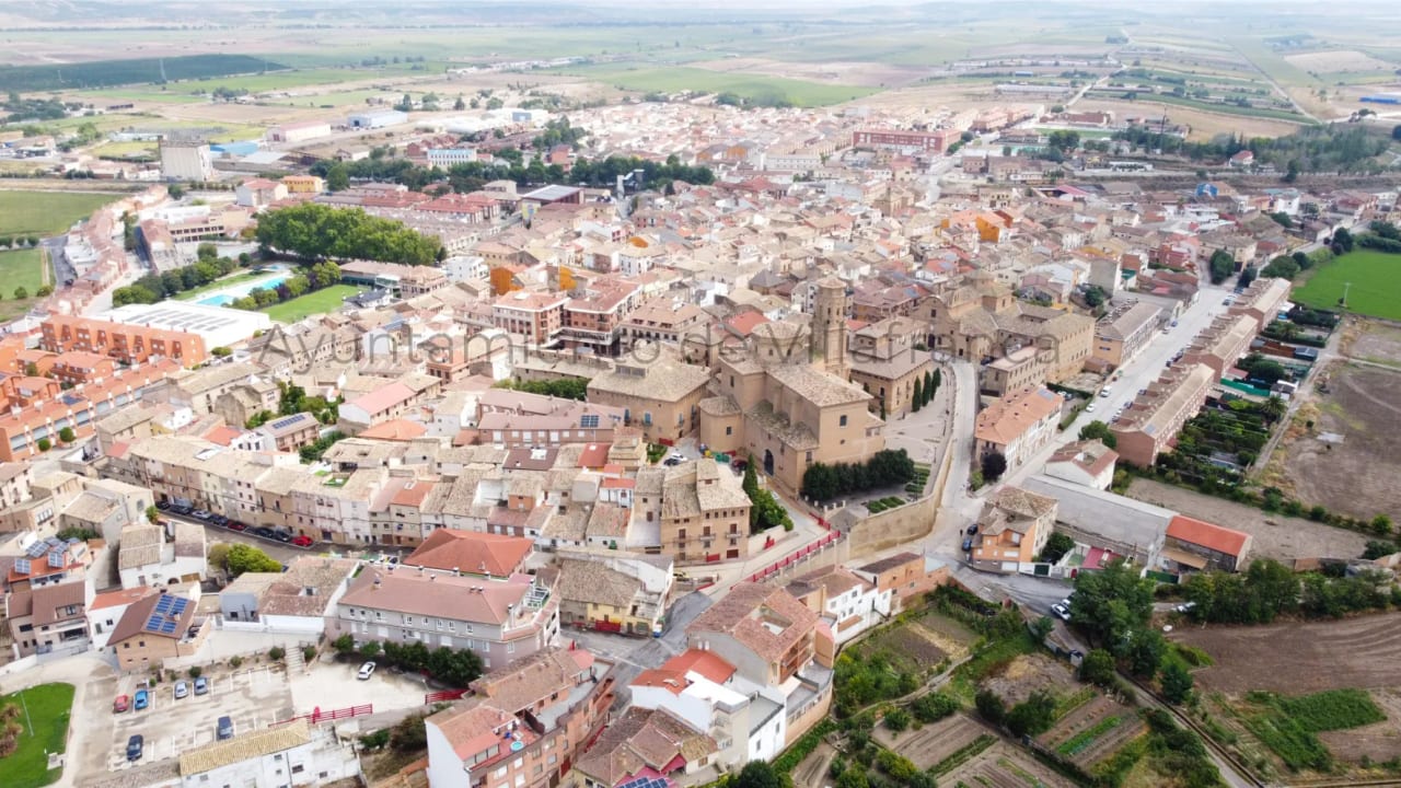 Vista aérea de una ciudad con edificios de techos rojizos y campos verdes.