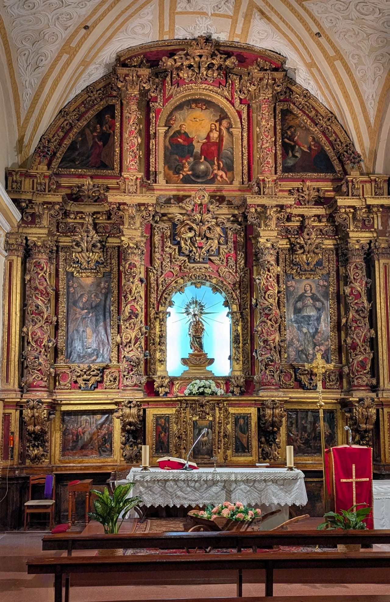 Retablo barroco con ornamentos dorados y rojo, con pinturas y esculturas de figuras religiosas.