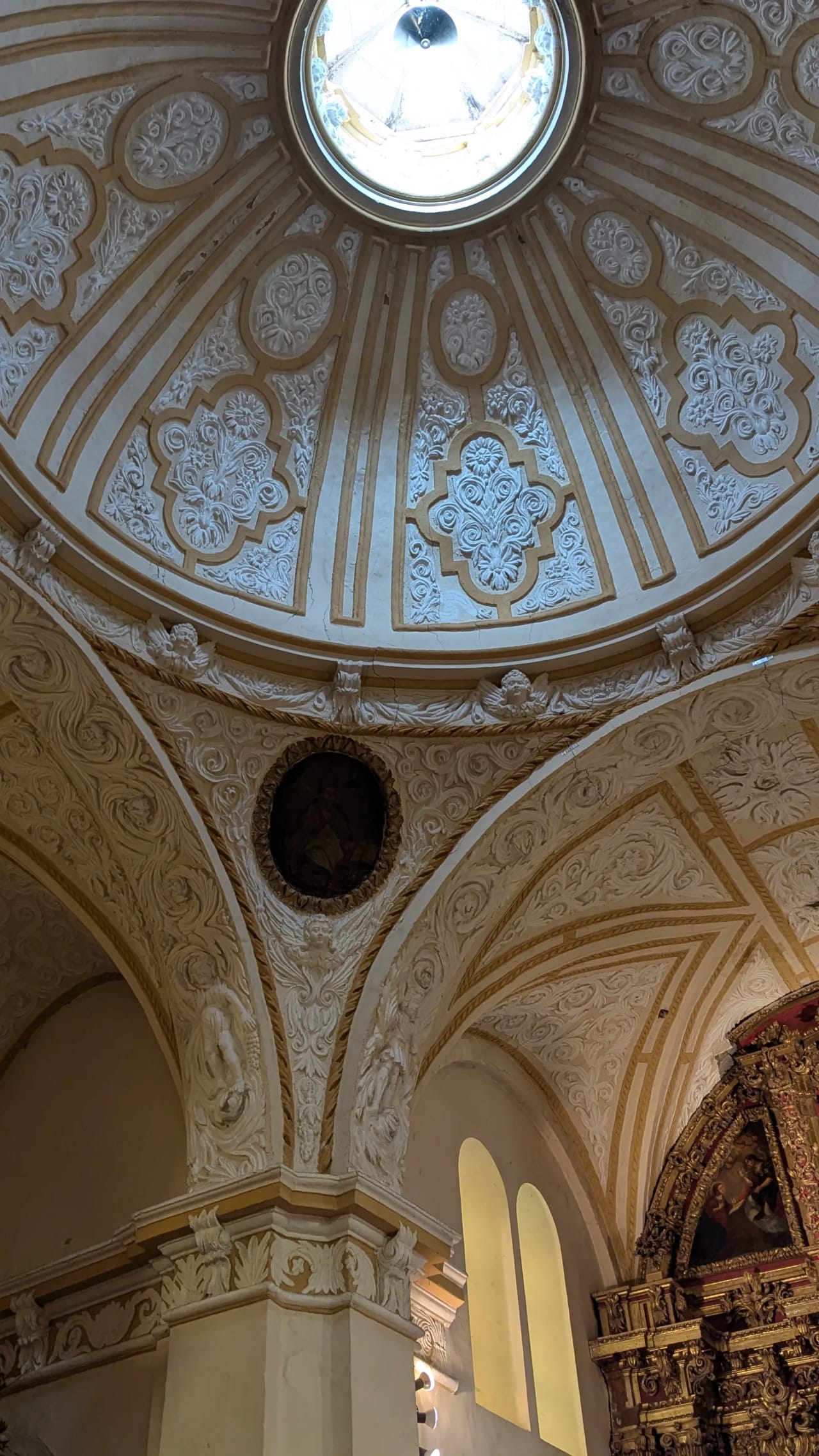 Cúpula de iglesia con detalles ornamentales y frescos, y una ventana en el techo.