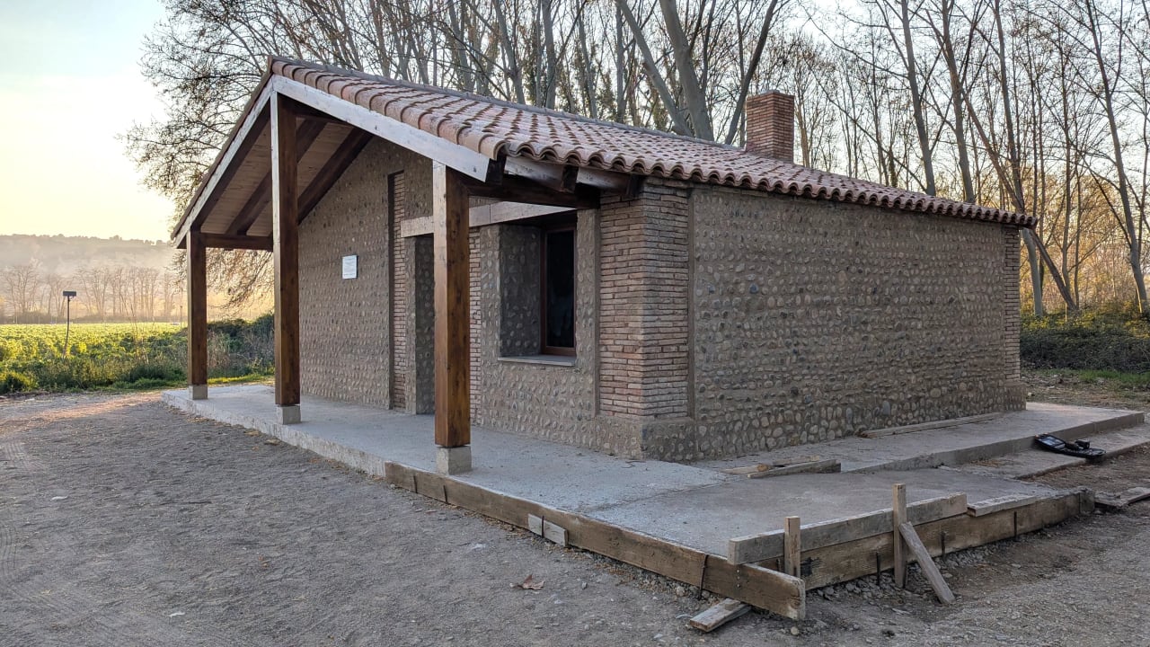Una pequeña casa de piedra con techo de tejas y porche en un área rural.