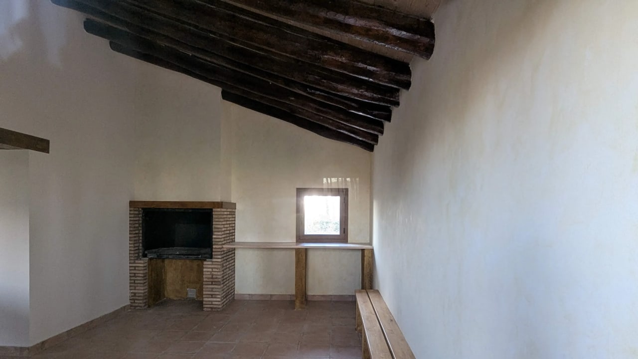 Habitación con chimenea de ladrillos, techo de vigas de madera y ventana.