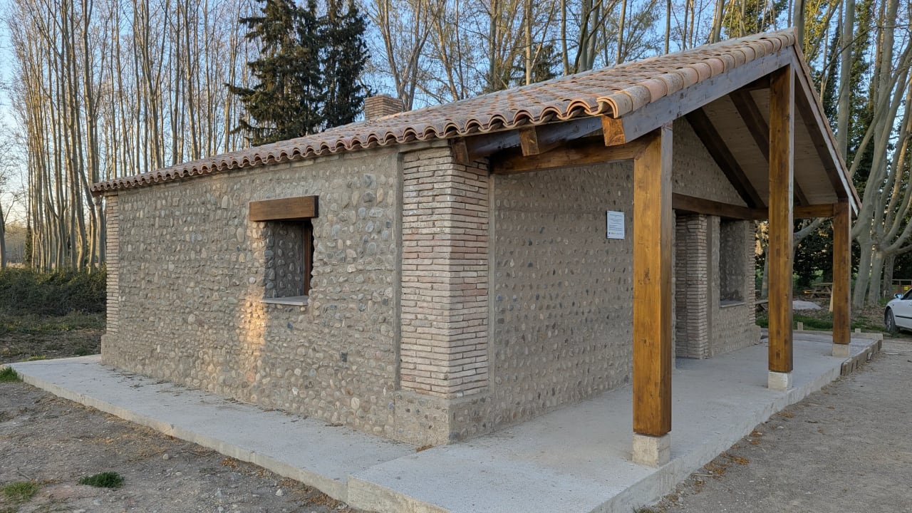 Una pequeña construcción de piedra con tejado de tejas y porche con pilares de madera.