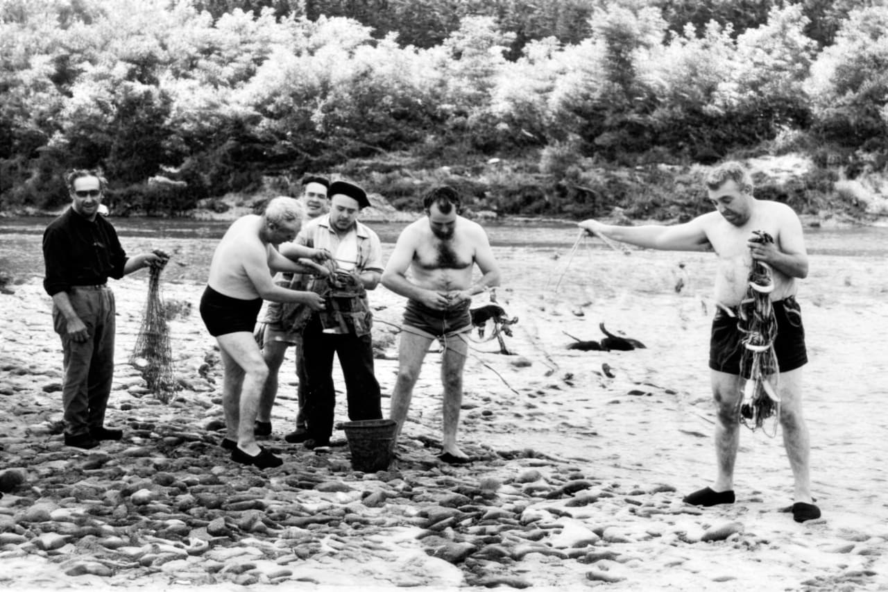 Hombres en una playa, algunos con redes de pesca y otros preparando equipo.