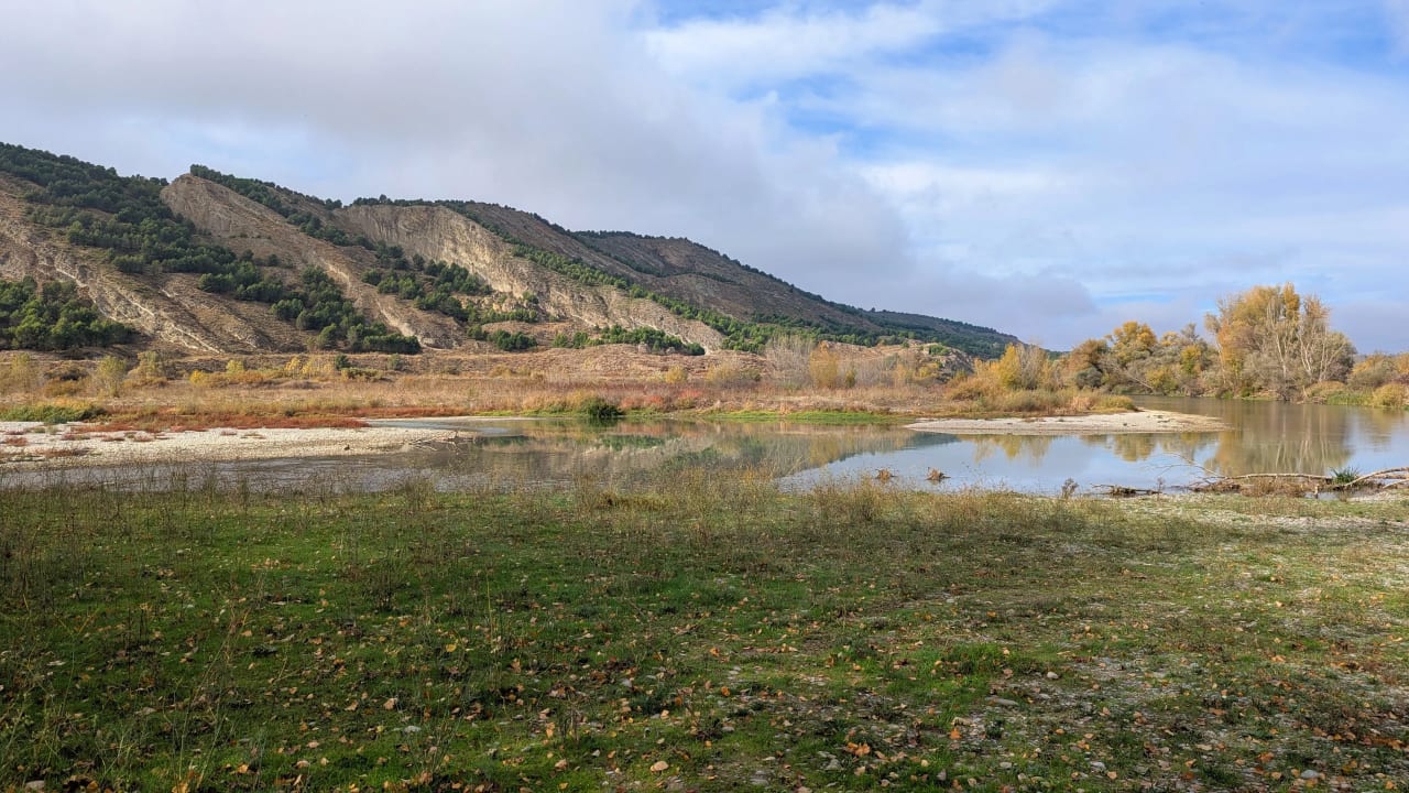 Un río tranquilo rodeado de montañas y vegetación en otoño.