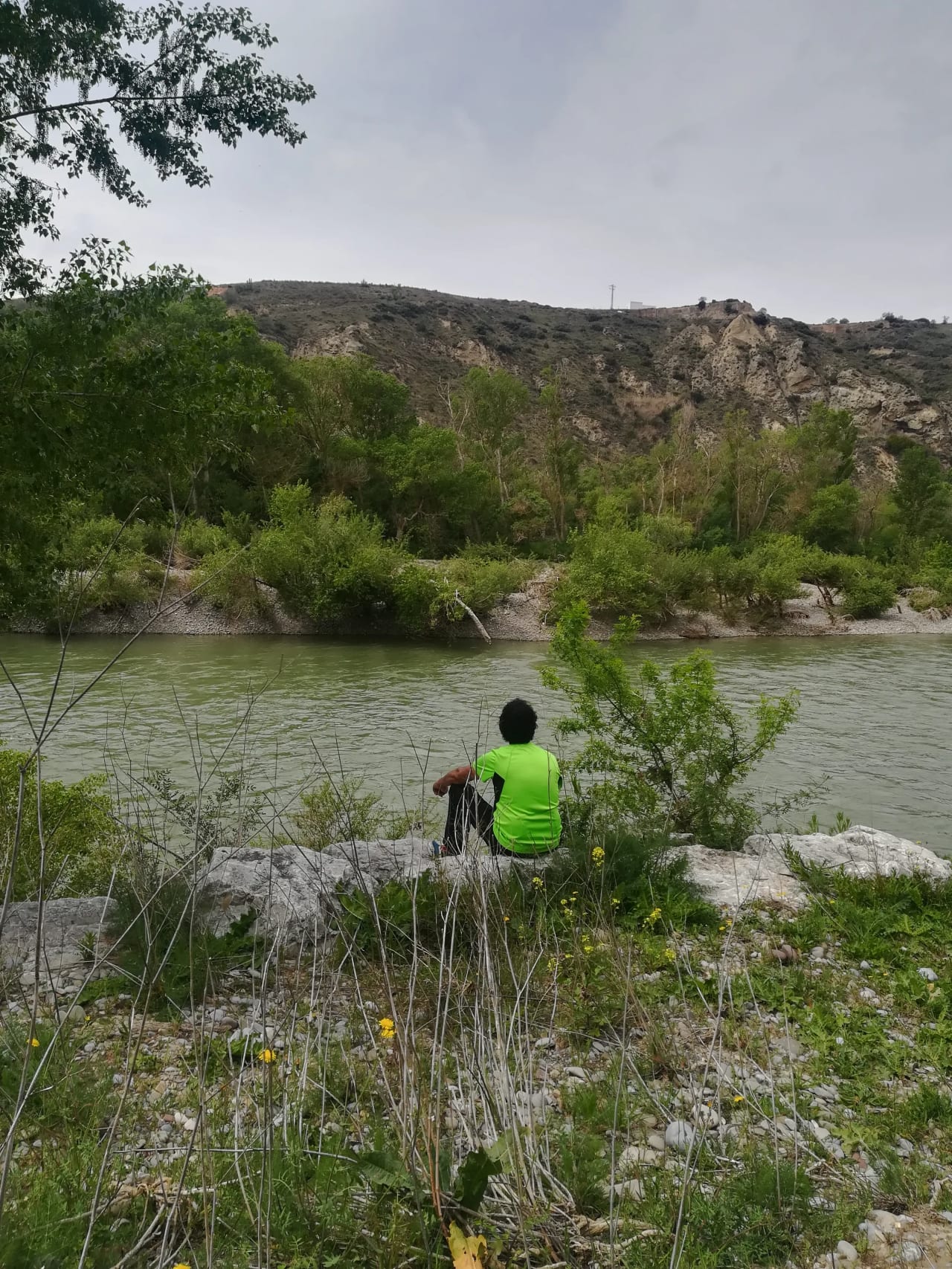 Un hombre sentado en una roca junto a un río, mirando hacia el agua.