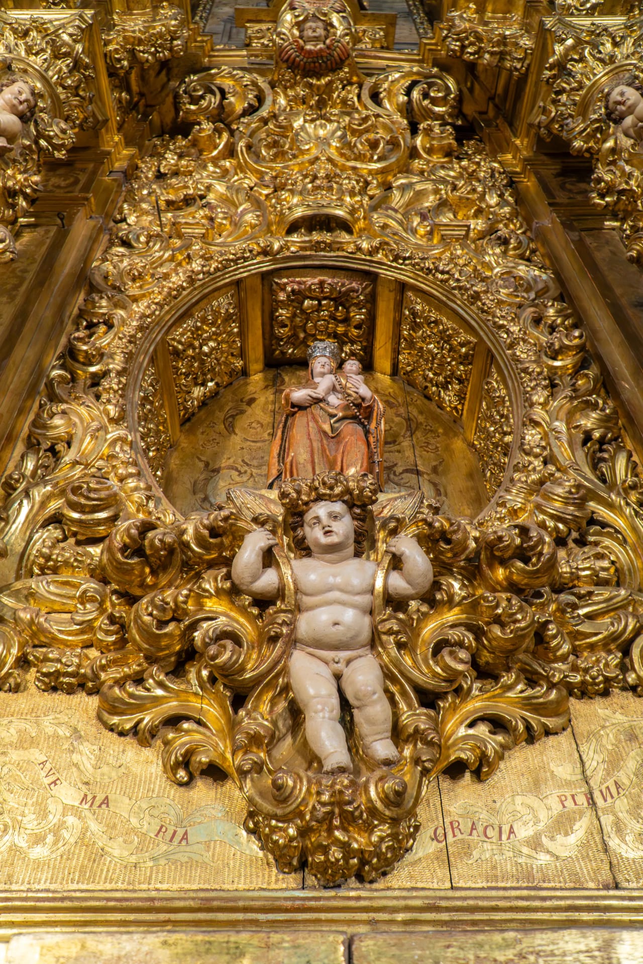 Escultura dorada de la Virgen María con el niño Jesús y un ángel.