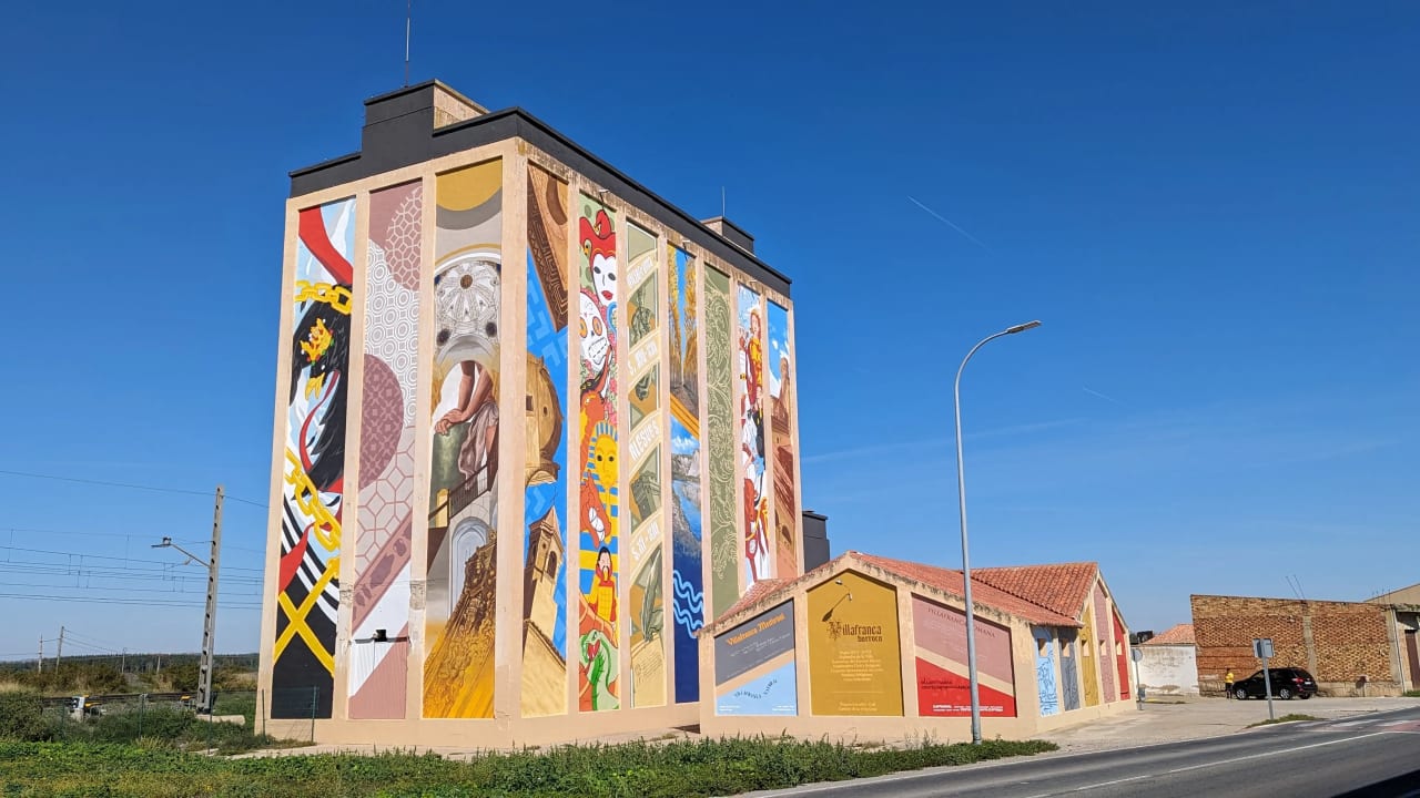 Mural colorido en una pared alta de un edificio junto a una carretera.