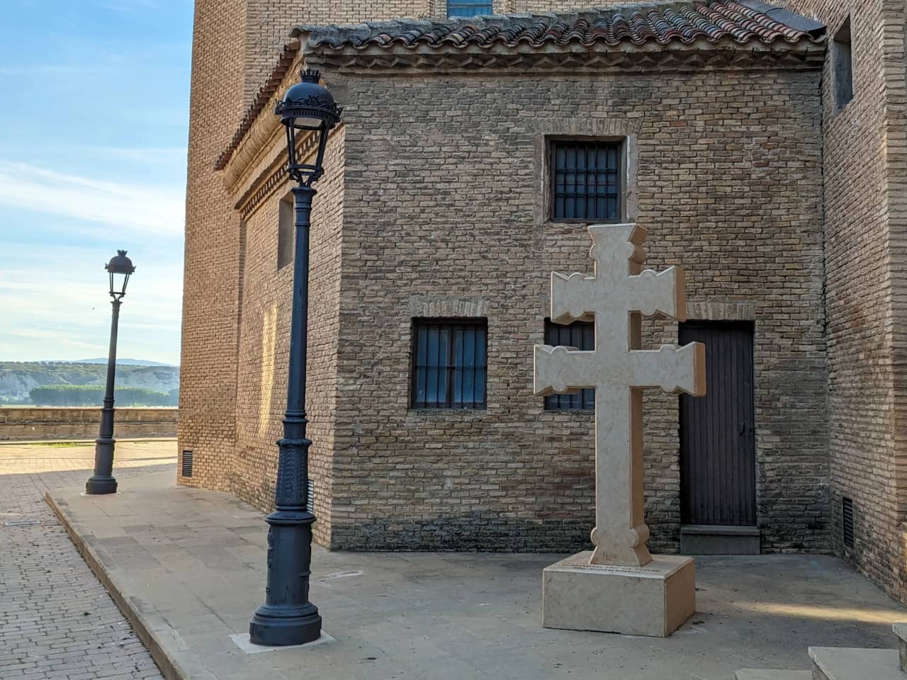 Cruz de piedra frente a un edificio de ladrillo en un entorno histórico