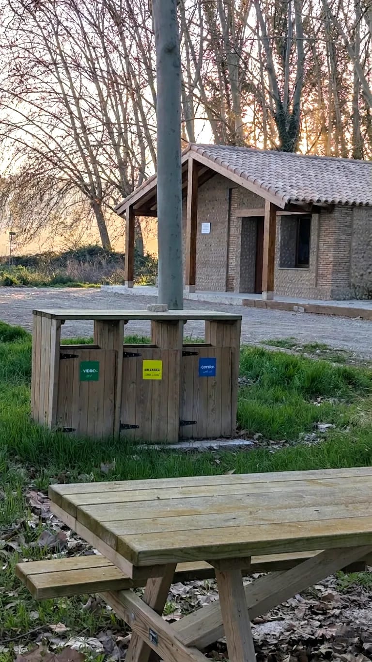 "Mesa de picnic con contenedores de reciclaje en un área verde."