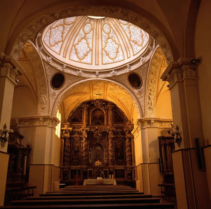 Interior de iglesia con techo abovedado y altar dorado.