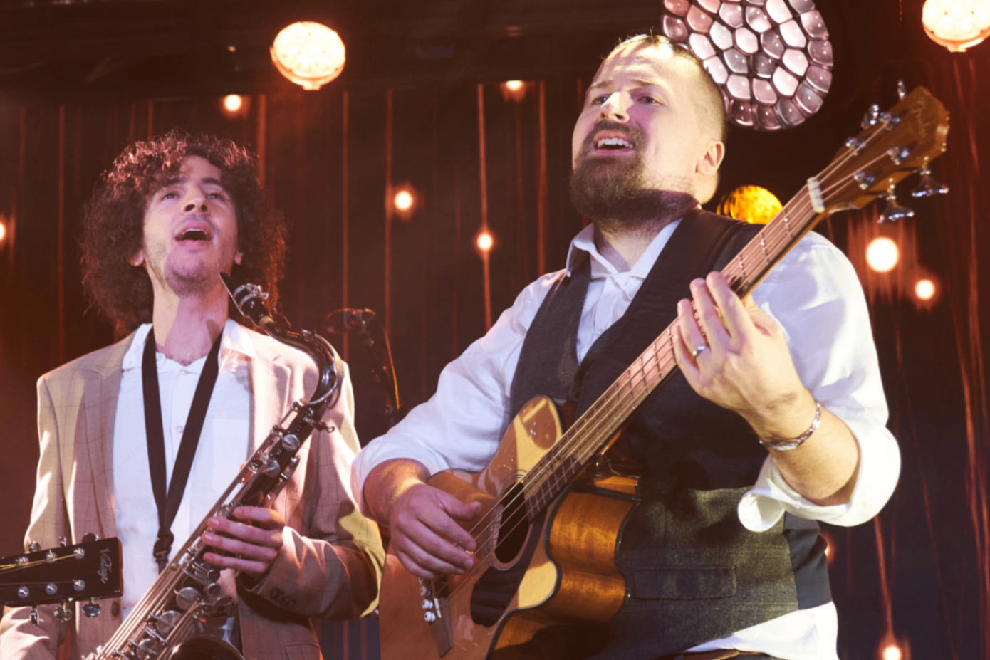 Fox & The Hounds: Acoustic guitarist and saxophonist performing together beneath warm stage lights
