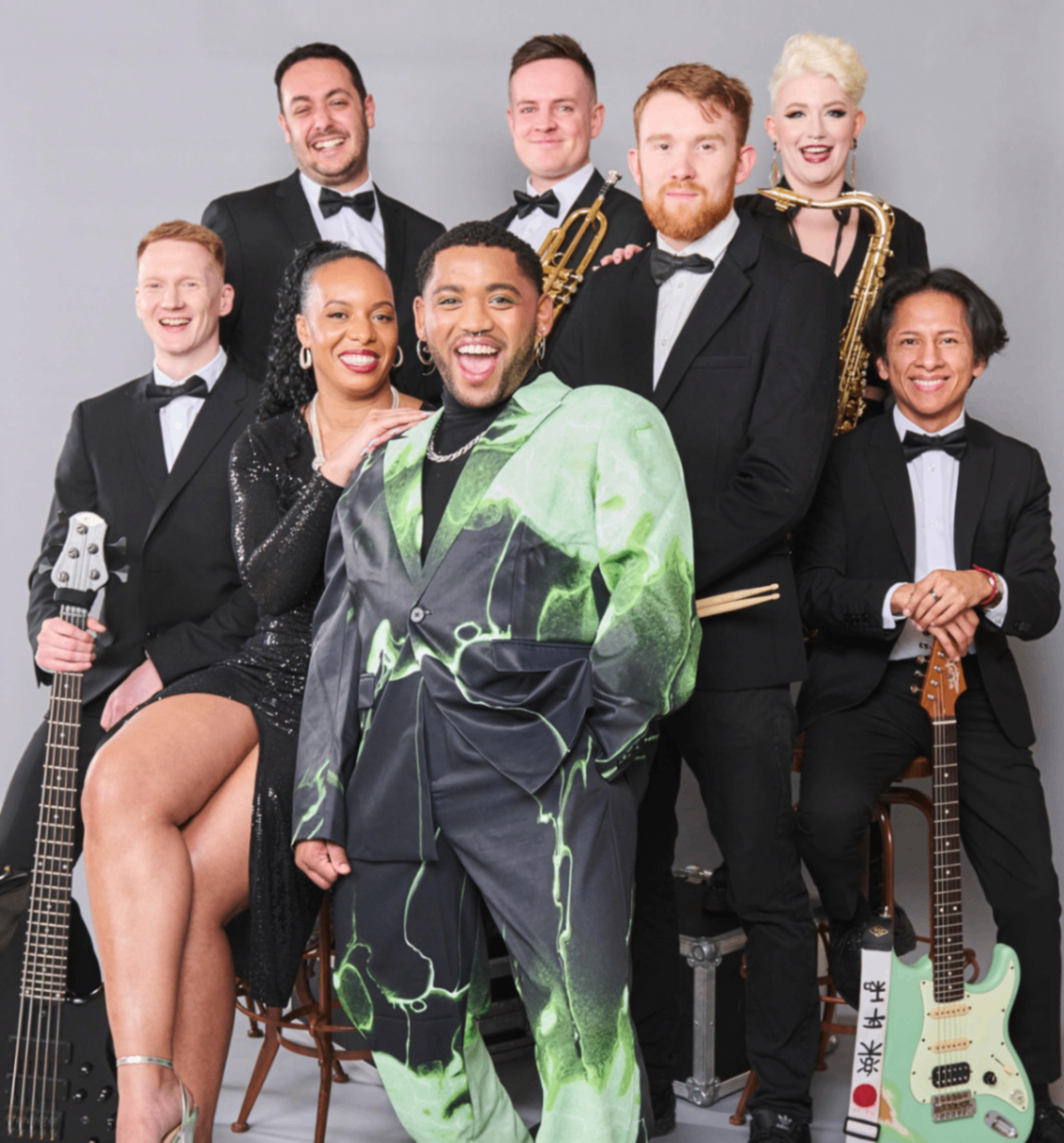Funk Royale: Eight band members posing in formalwear with guitars and a saxophone against a grey backdrop