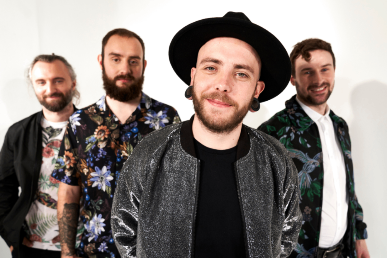 High Voltage: Four band members posing against a white background, with a guitarist in a black hat at the front