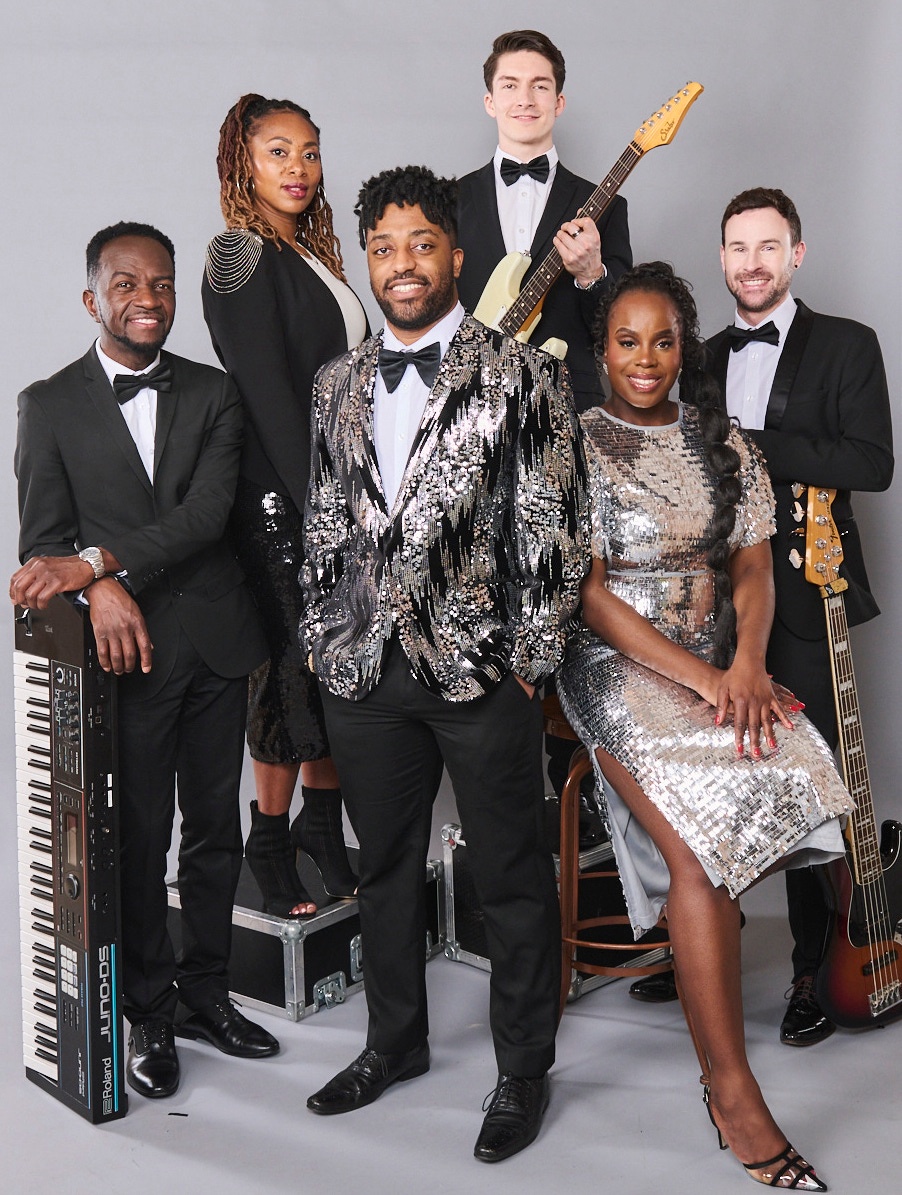 Committed to Kisstory: Six band members posing with a keyboard and guitars against a grey studio backdrop