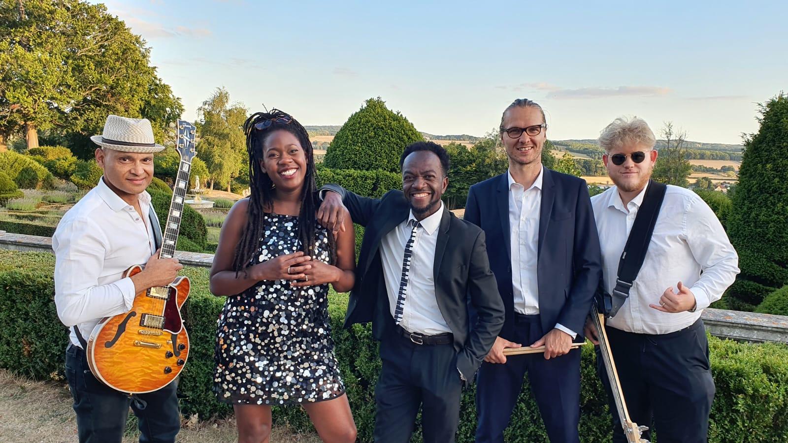 One Love: Five band members posing outdoors in a landscaped garden with a guitarist holding his instrument