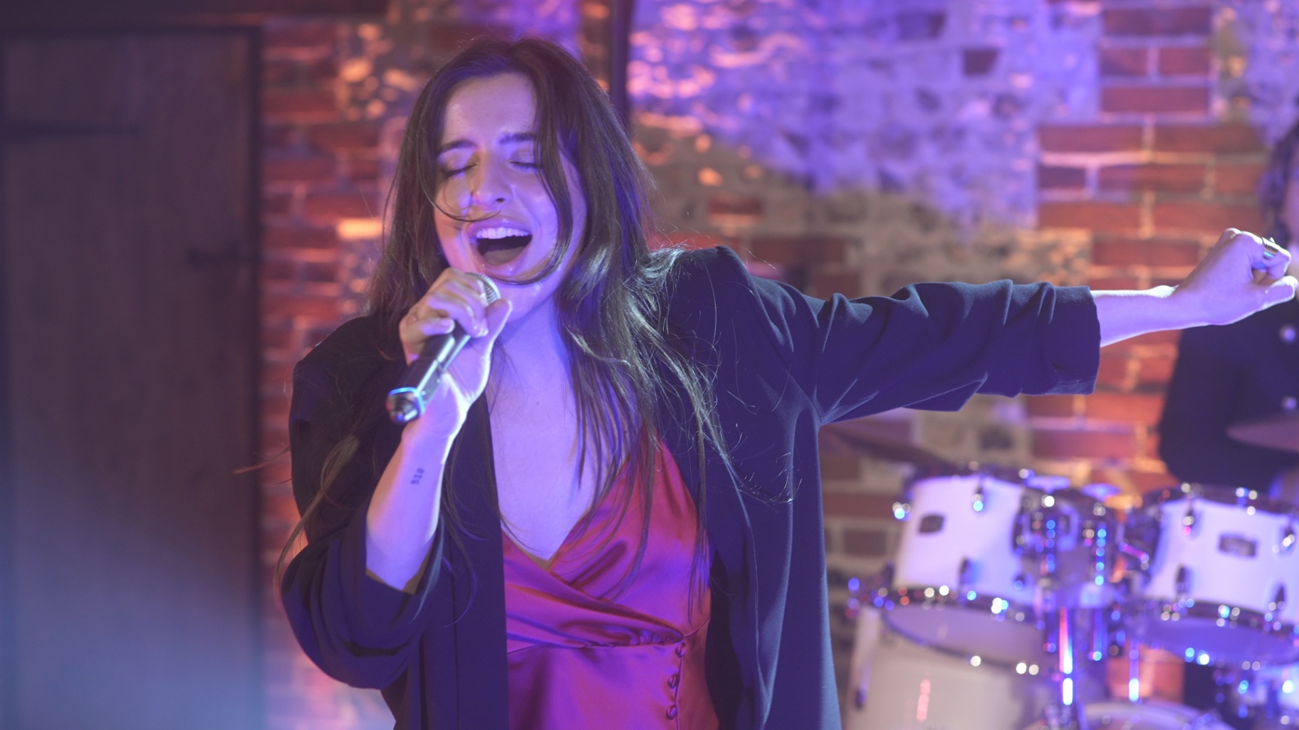 Band Salsa: Vocalist singing with one arm extended in front of the drum kit