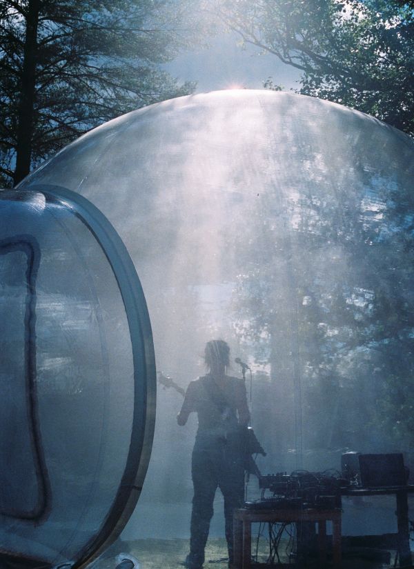 A person plays guitar inside a transparent bubble with sun light glistening down