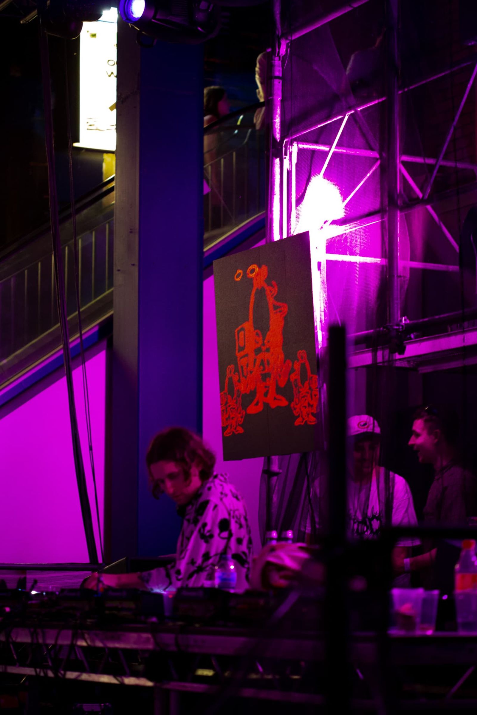 Mall grab DJing in front of scaffolding with square LED panel attached showing naughty looking character holding gun with smoke coming from it (bad tunes logo) in red.