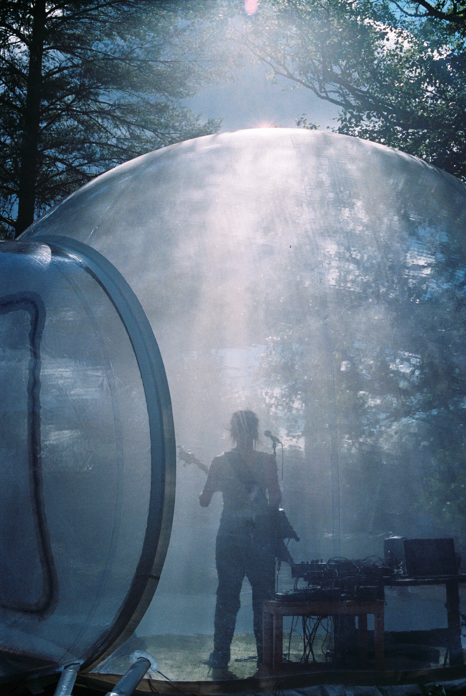 A person plays guitar inside a transparent bubble with sun light glistening down