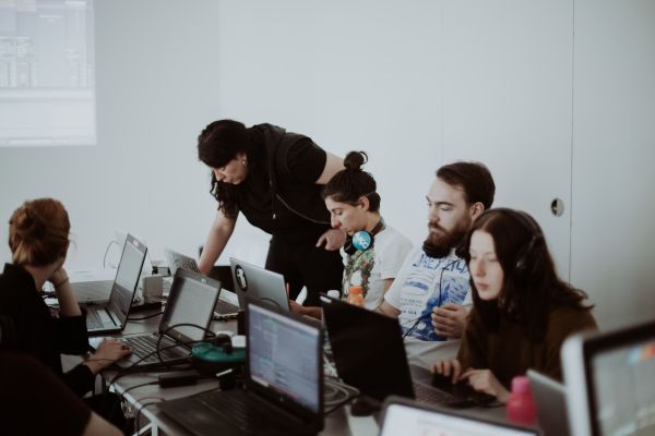 Several people sit on laptops on a table learning music production