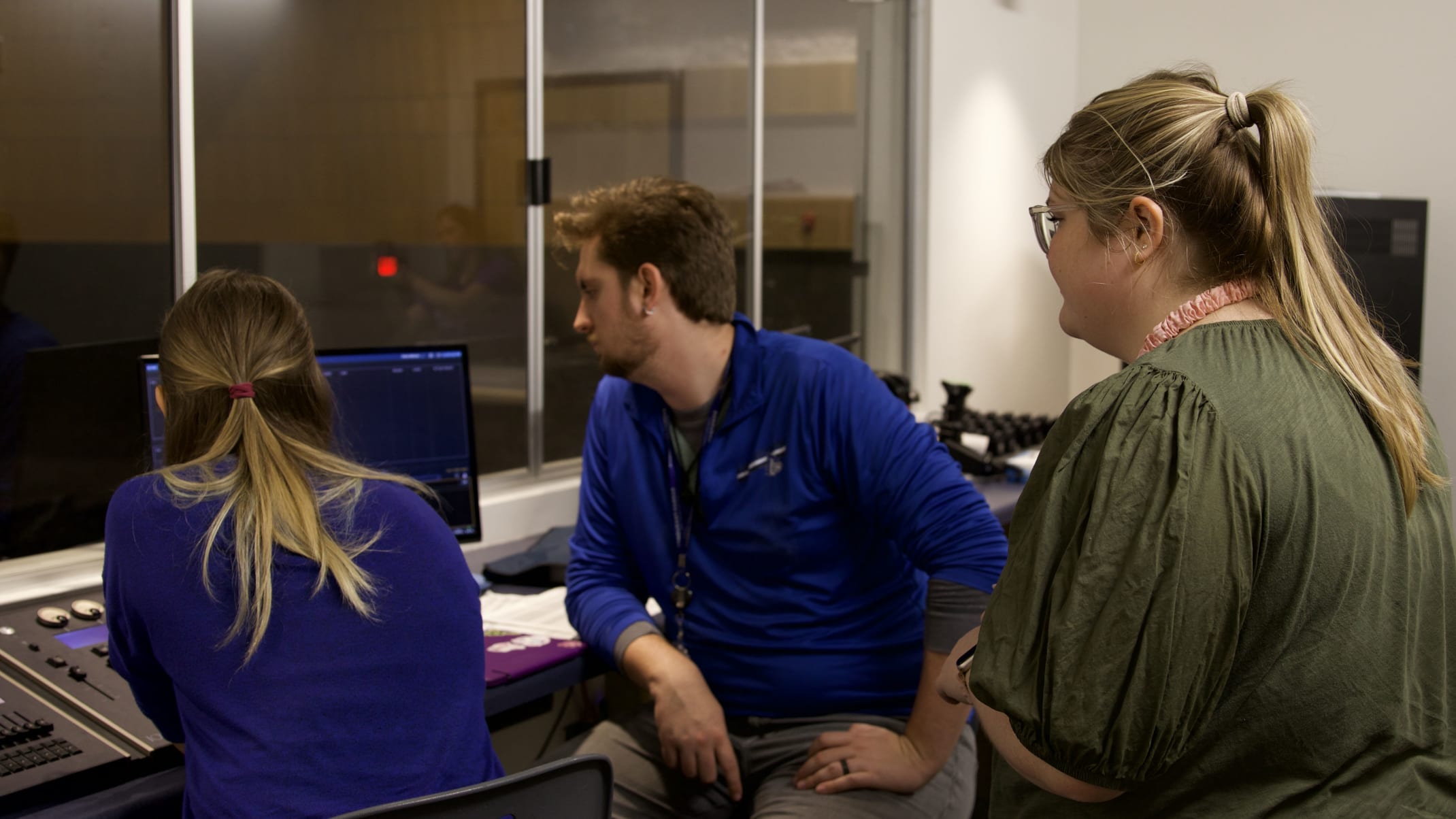 The image shows three people, two women and one man, sitting in front of a computer screen in what appears to be an office or workspace setting.