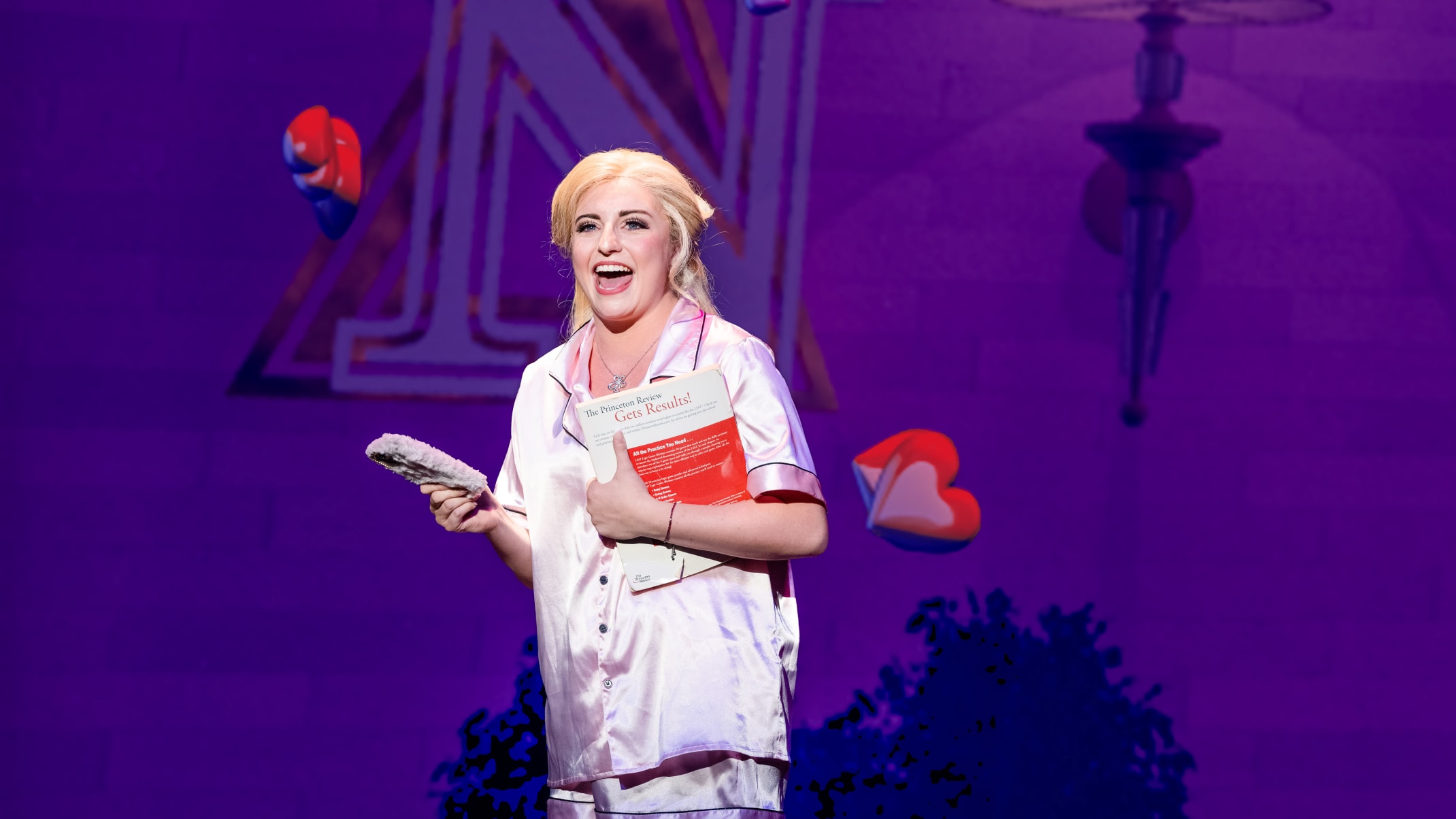 A blonde woman (Elle) standing and singing.