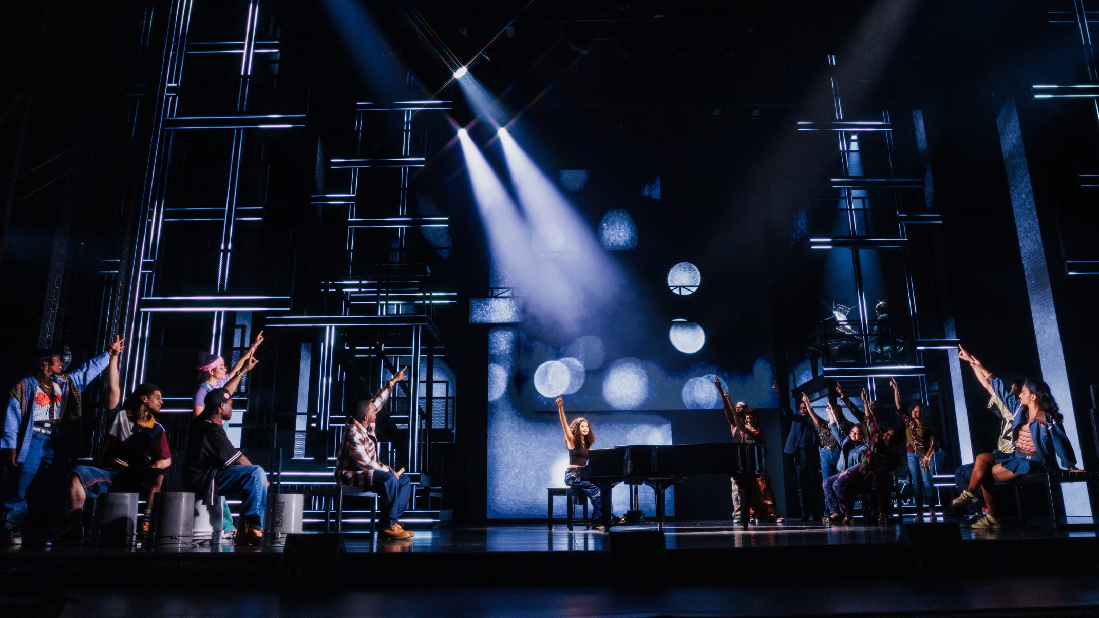 A large group of people enthusiastically singing and dancing on stage with bright lights.