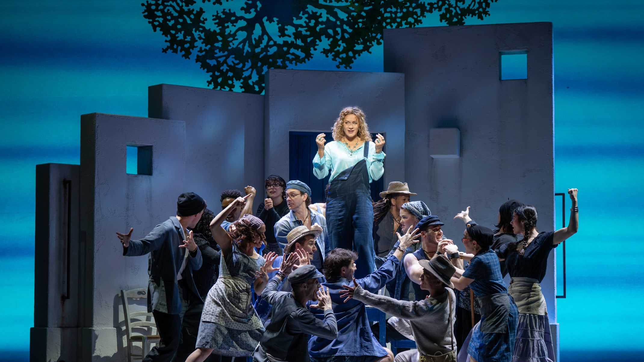 Photo of one woman singing in a spotlight surrounded by a group of other people more dimly lit