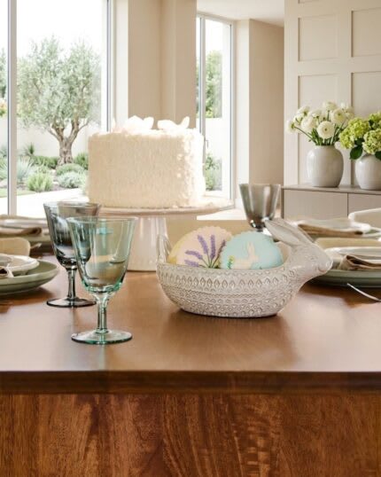 Elegant wooden dining table setup with dessert, glassware, and table decor in a bright modern dining room