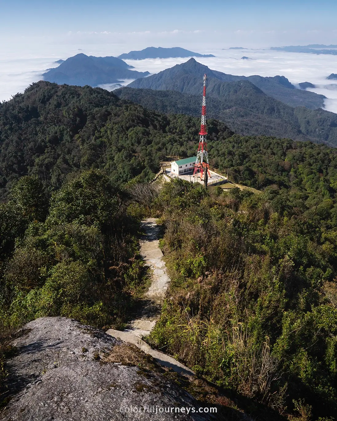 A radio tower surrounded by a mountain range covered in a blanket of clouds.