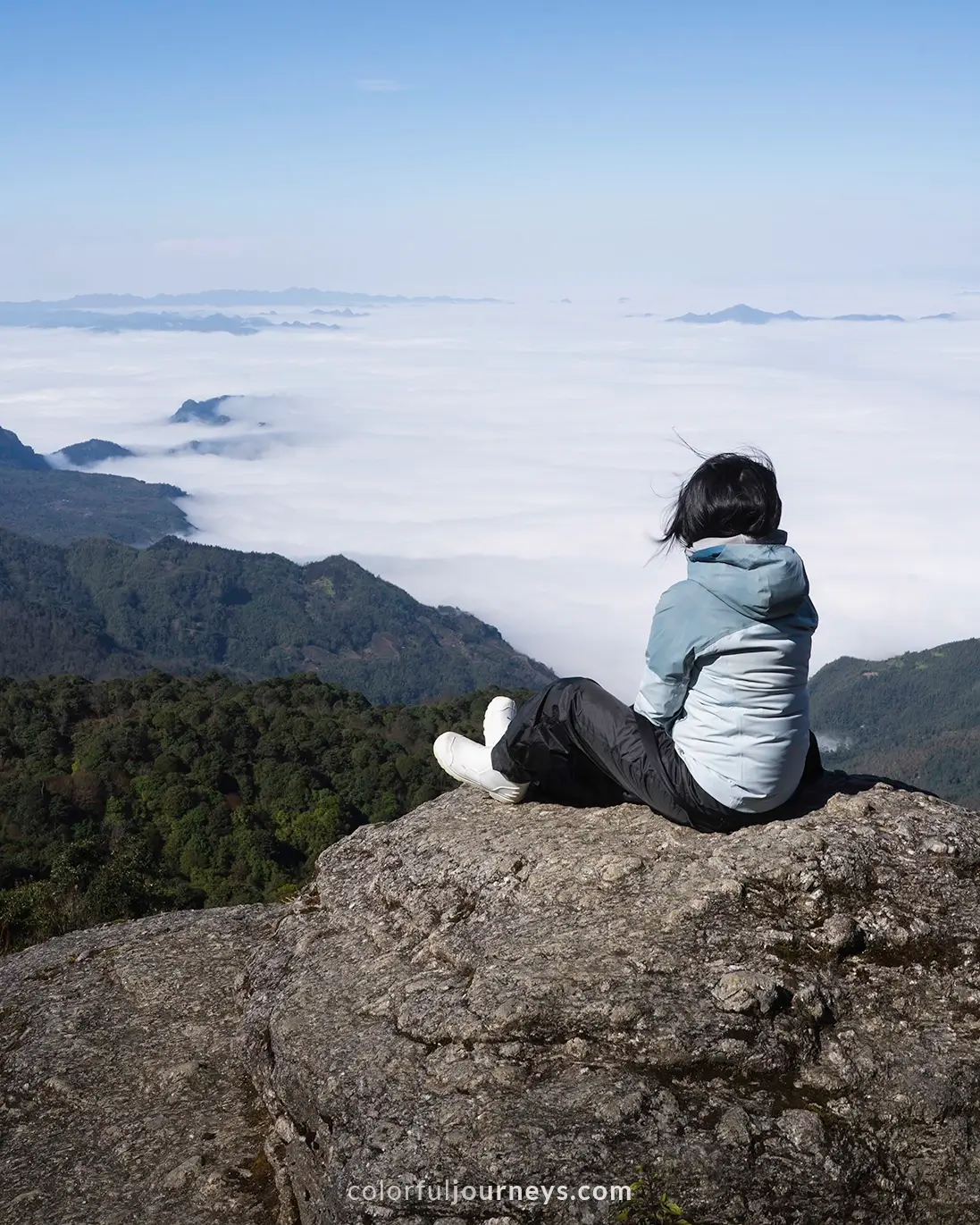 A woman looks into a mountain range covered in a blanket of clouds.