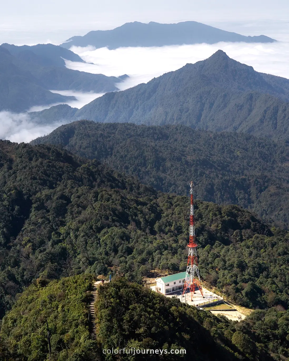 A radio tower surrounded by a mountain range covered in a blanket of clouds.