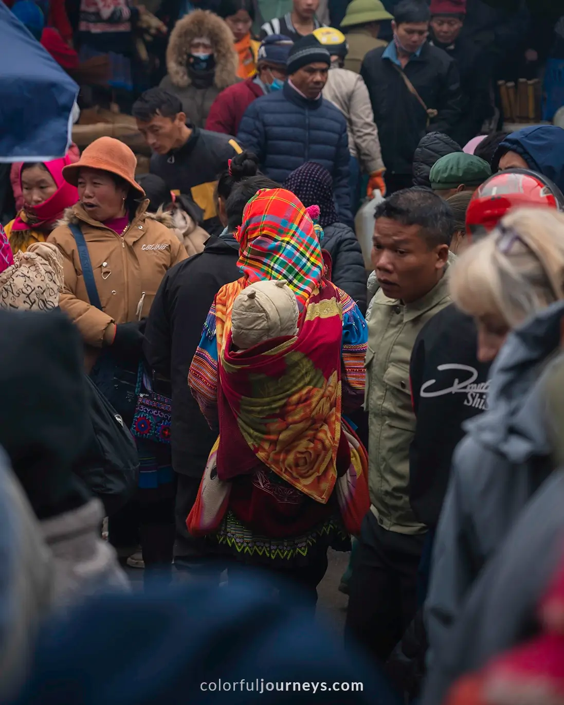 A woman wearing colorful clothes carries her baby through the busy Bac Ha market, Vietnam