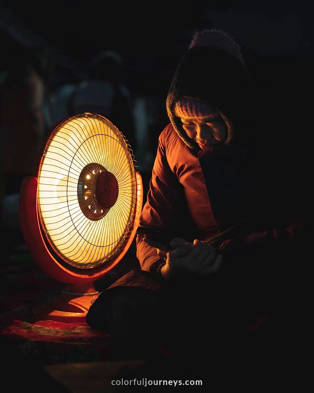 A woman heats up next to a heater at Bac Ha market, Vietnam