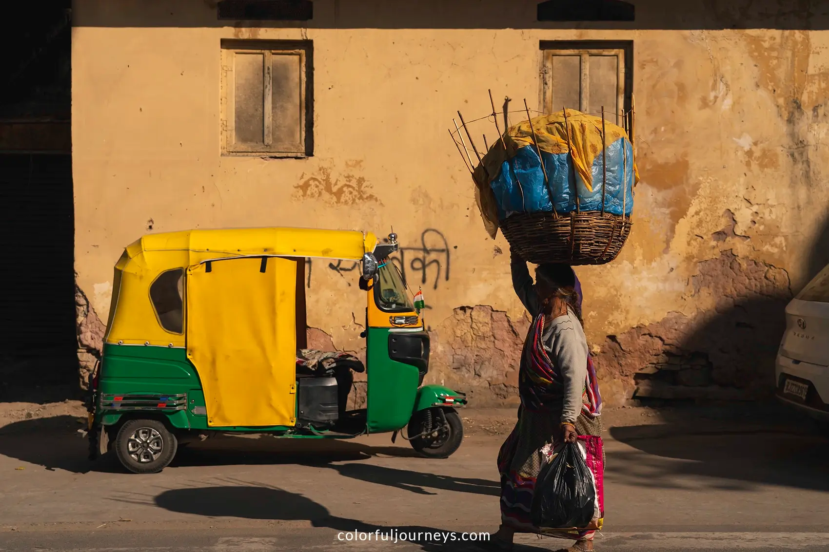 A woman carrying goods on her head walks past an auto-rickshaw in Jaipur, India