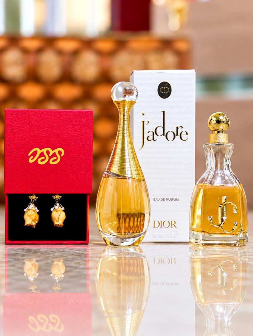 Gold drop earrings in a red gift box beside two luxury perfume bottles