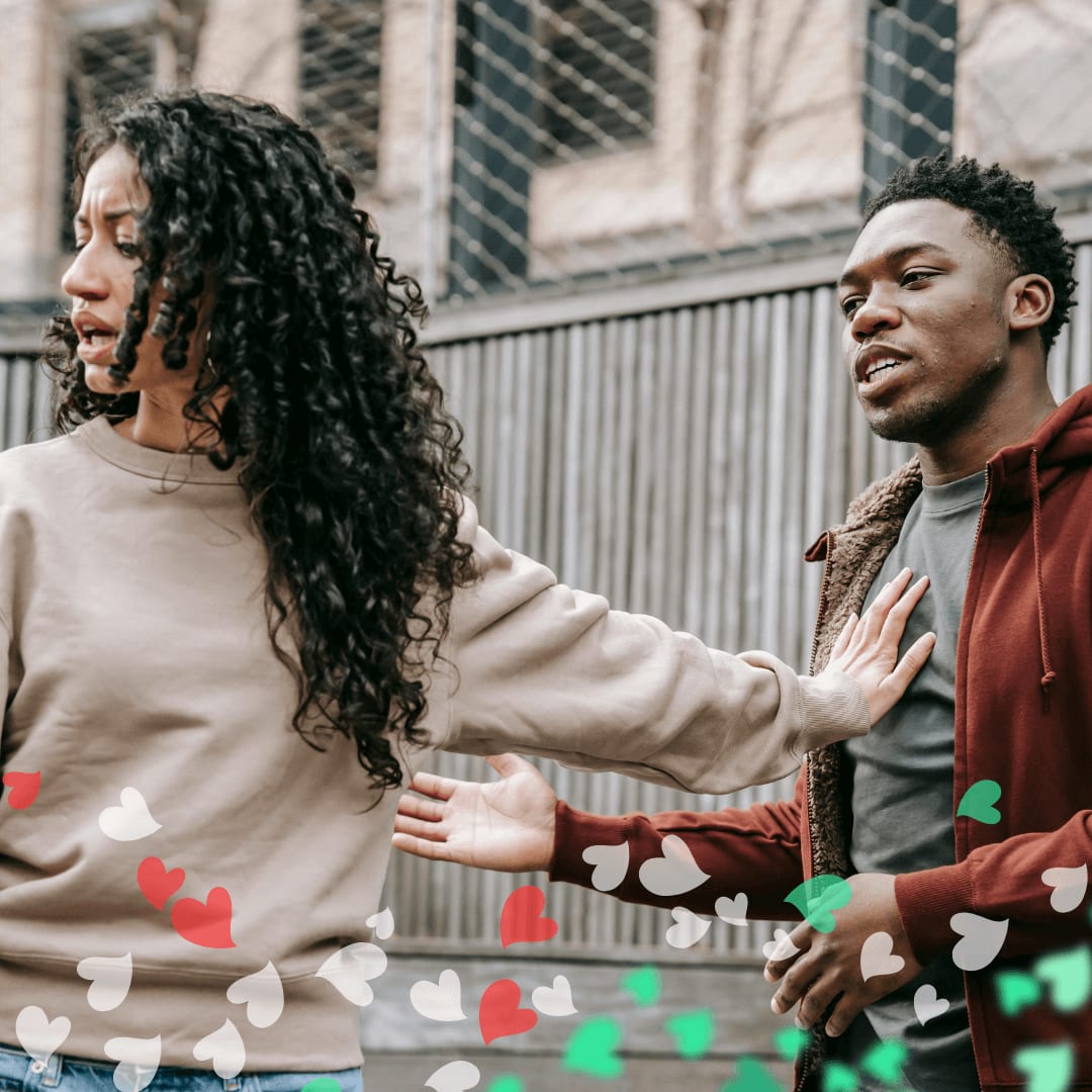 A woman with curly hair extends her arm to keep distance from a man talking to her outside near a fence. Heart-shaped graphics are overlaid, hinting at heartbreak in the midst of love.