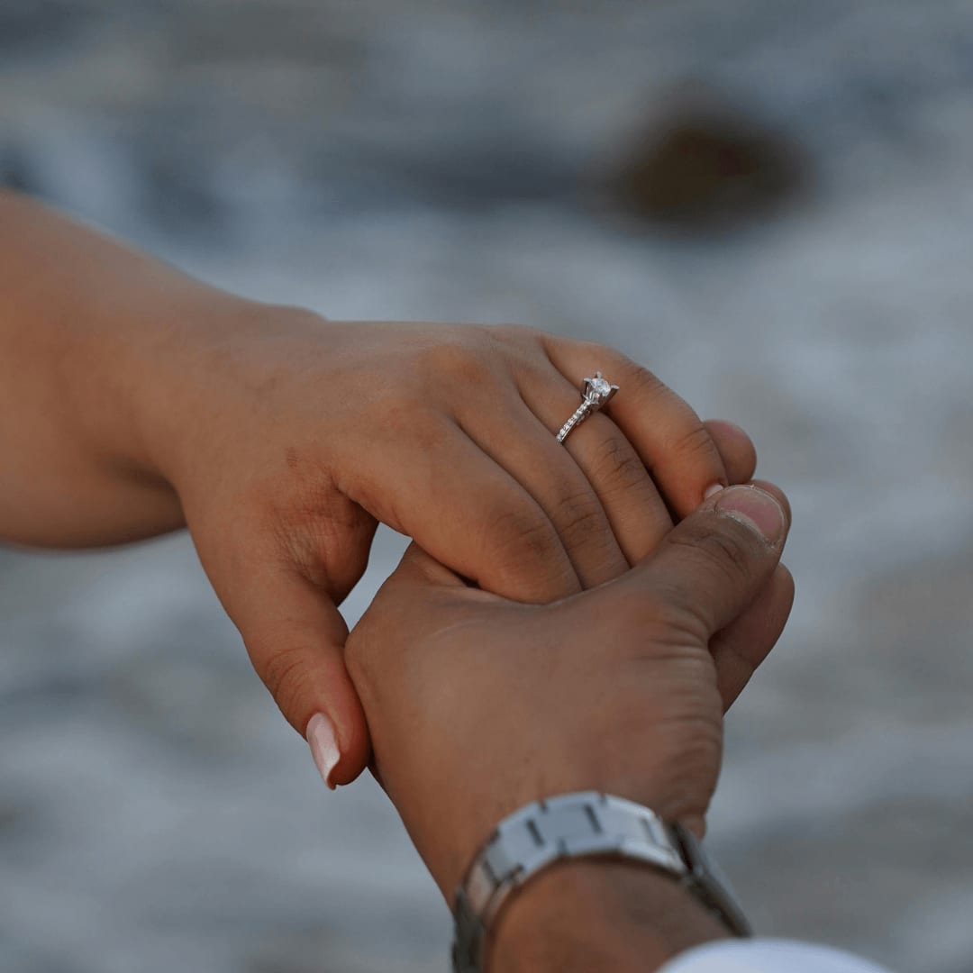 Close-up of a couple holding hands with a focus on an engagement ring on the woman's finger, embodying love and commitment.