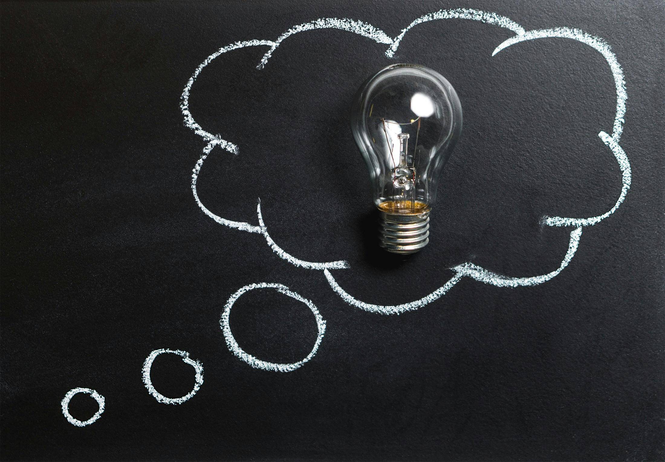 Light bulb placed on a chalkboard with a thought bubble drawn around it, symbolizing creativity, ideas, and learning.