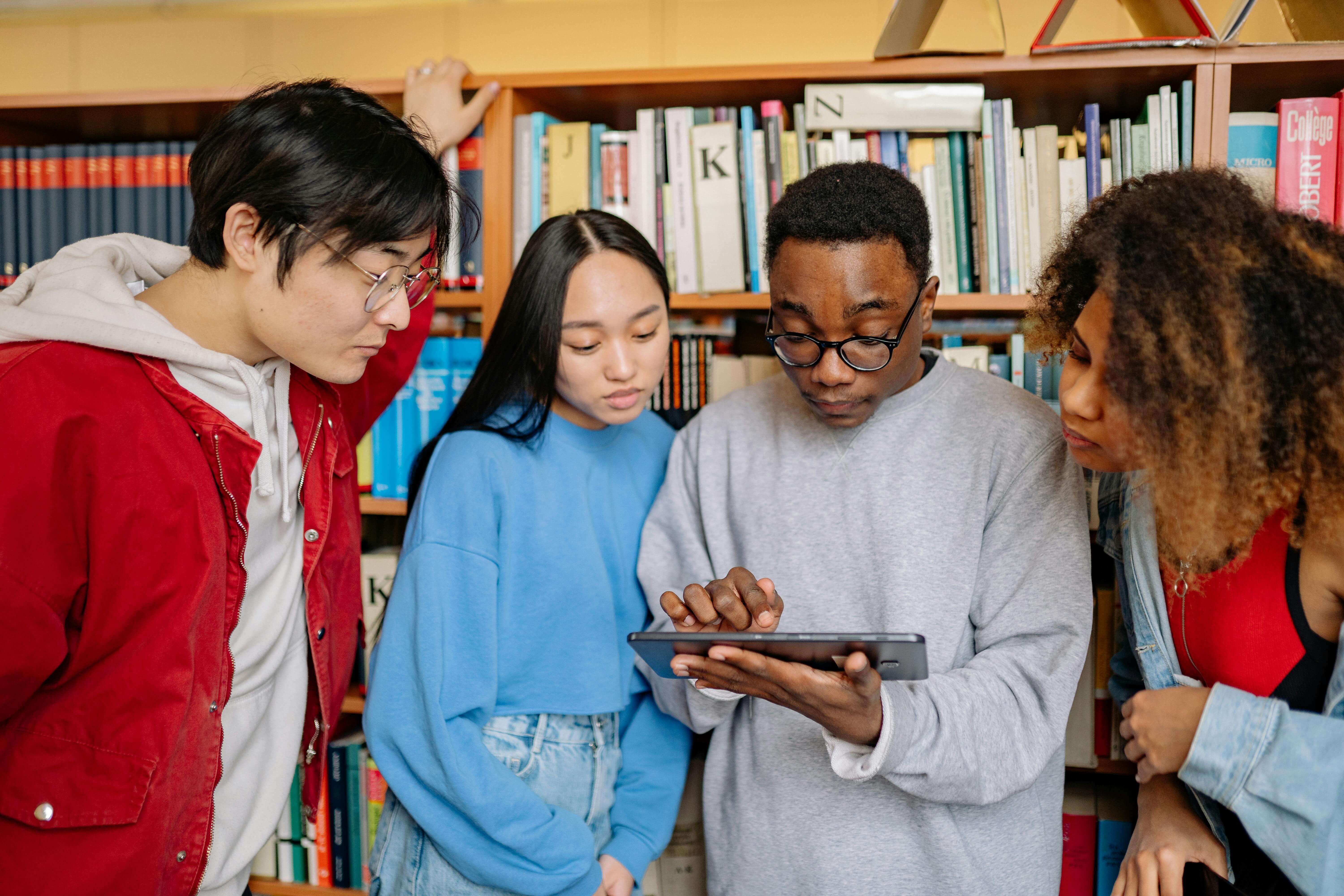 Group of students collaborating on a tablet in a library – conveys community learning and mirrors the table's discussion of free tools.