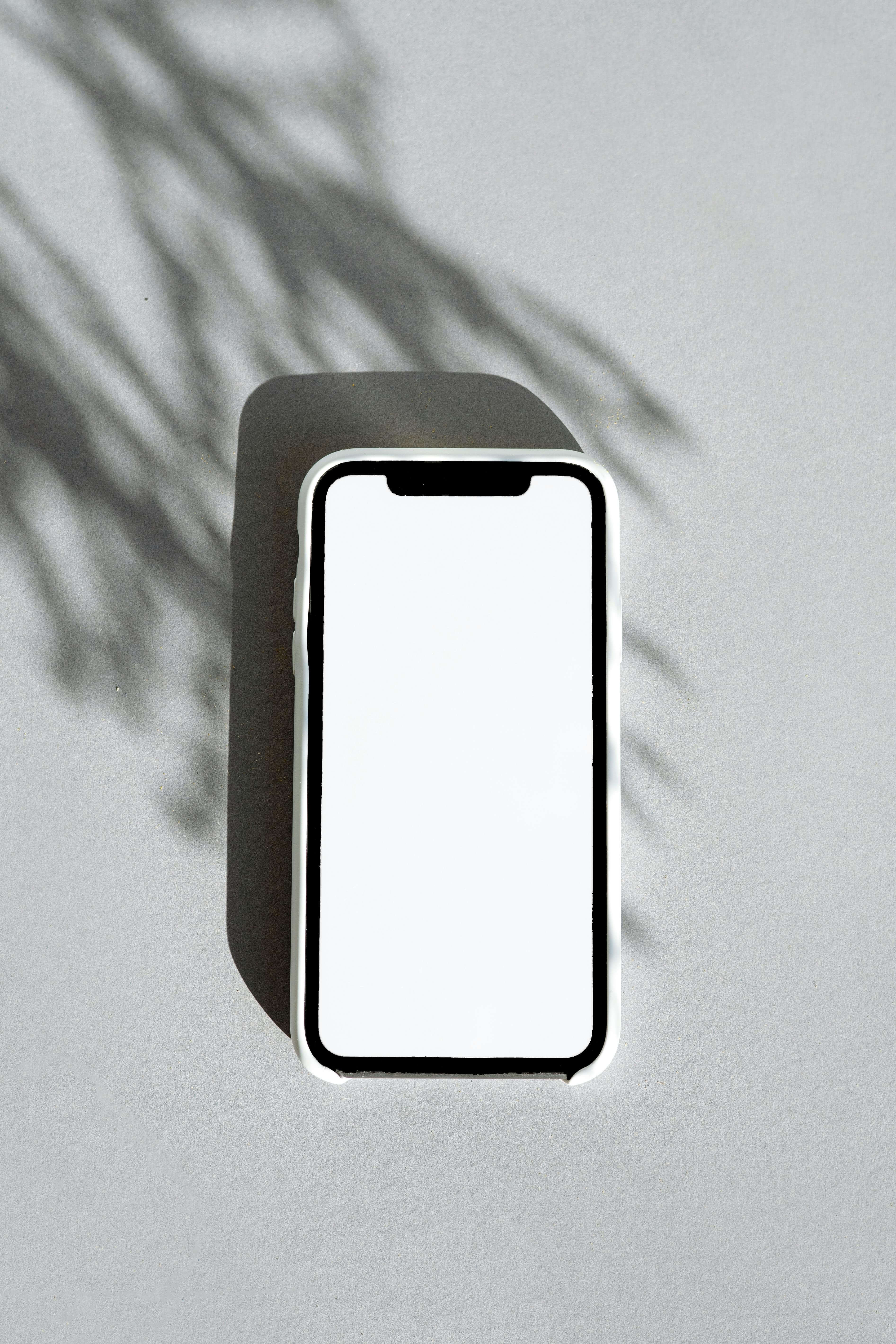 A blank white smartphone lying on a gray surface with soft shadows—illustrates mobile‑first flashcard apps and on‑the‑go studying.
