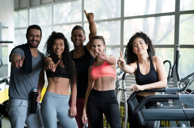 Un grupo de participantes en una clase de acondicionamiento posando juntos en un gimnasio. (Compromiso en un estudio de fitness)