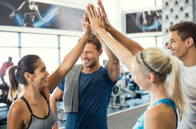 Un grupo de amigos chocando los cinco en un estudio de fitness, celebrando un logro de entrenamiento. (Ideas para eventos en estudios de fitness)